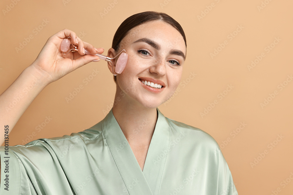 Beautiful young woman doing facial massage with roller on beige background Beautiful young woman doing facial massage with roller on beige background