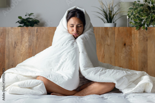Fotografi Tired and cold woman covered with the duvet sitting on the bed at home