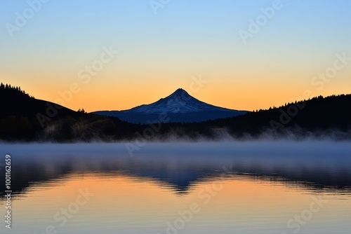 A tranquil lake reflects the stunning silhouette of a snow-capped mountain during a peaceful early morning at dawn