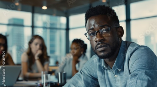 A thoughtful man, seated in a bright office, gazes attentively at a colleague, portraying focus and engagement in an important meeting.