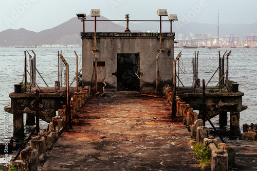 Abandoned pier covered in red rust sitting on the bank of a city harbour in the evening photo