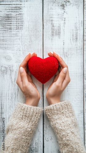 Gentle hands cradle a vibrant red heart against weathered white wooden planks, symbolizing love, care, and compassion in a rustic, heartwarming setting. photo