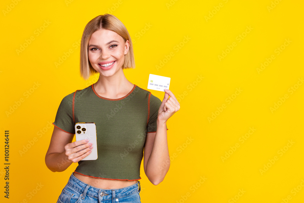 Photo of cheerful girl with bob hairdo dressed khaki crop top hold smartphone show credit card isolated on yellow color background Photo of cheerful girl with bob hairdo dressed khaki crop top hold smartphone show credit card isolated on yellow color background