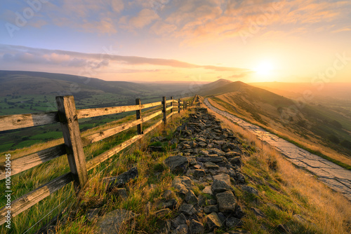 Golden sunrise at Mam Tor with footpath leading along ridge in The Peak District, UK.