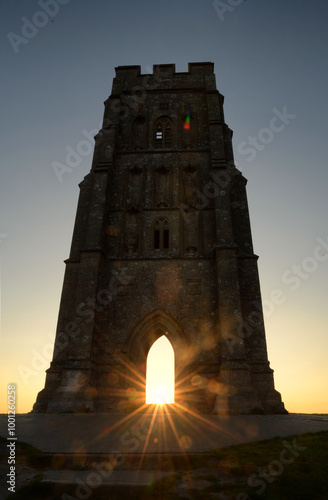 Sunburst through the archway of a historic Glastonbury Tor tower at sunrise