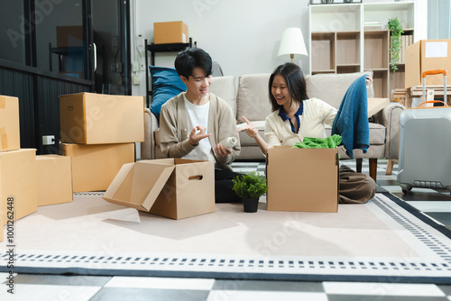 Young couple relaxing sitting on the floor around cardboard boxes at home, smiling happy moving to a new house.