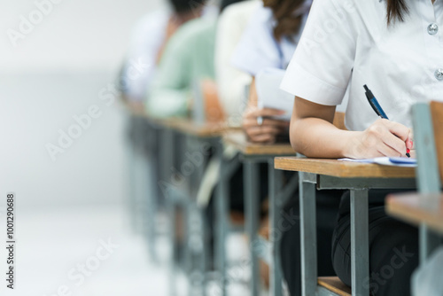 Students Taking Exam in Classroom Setting. Students in uniforms are seated in a classroom, writing answers during an exam, highlighting focus and academic testing. photo