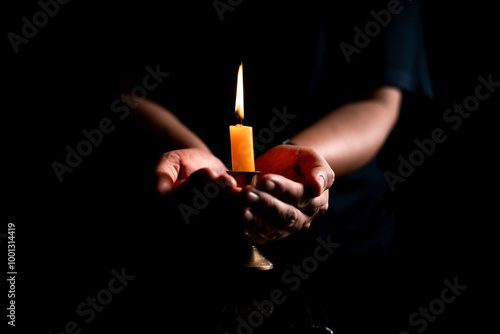 In the dark, hand clasped in prayer, illuminated by the soft candlelight, as black flames of candle fire flickered gently. candle, pray, hand, prayer, black, fire, flames, candlelight, light, dark.