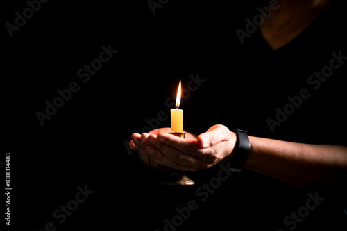 In the dark, hand clasped in prayer, illuminated by the soft candlelight, as black flames of candle fire flickered gently. candle, pray, hand, prayer, black, fire, flames, candlelight, light, dark.