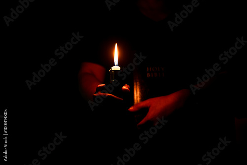 In the church, candle flickered beside cross as Christians gathered to pray, their faith in Jesus and spiritual devotion illuminated by Bible in background, deepening their Catholic worship.