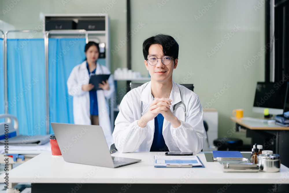Confident young male doctor in white medical uniform sit at desk working on computer Confident young male doctor in white medical uniform sit at desk working on computer