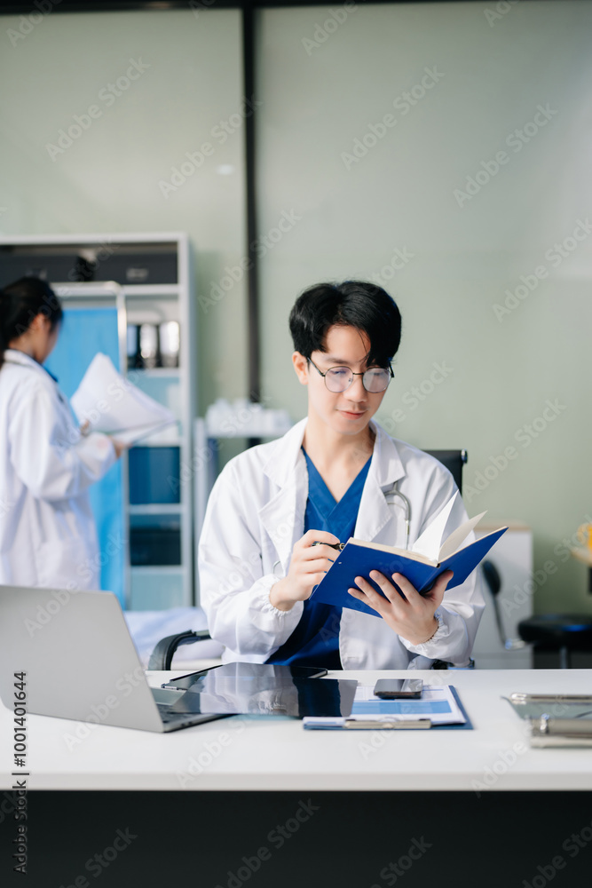 Confident young male doctor in white medical uniform sit at desk working on computer Confident young male doctor in white medical uniform sit at desk working on computer
