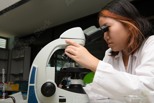 Cute scientist schoolgirl in lab coat looks through microscope for study microbiology in laboratory. photo