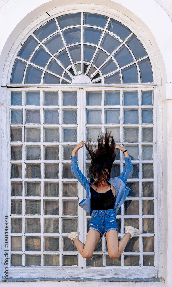 Young woman leaps by a large window. A young woman leaps joyfully near a grand window, her hair flying as she embraces the moment on a bright day. Young woman leaps by a large window. A young woman leaps joyfully near a grand window, her hair flying as she embraces the moment on a bright day.