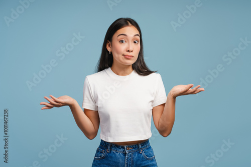 Bild auf Leinwand Confused young Asian woman shrugging with raised arms and open palms on blue bac