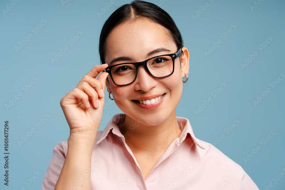 Asian woman wearing eyeglasses adjusting eyeglasses looking at camera, isolated on blue background Asian woman wearing eyeglasses adjusting eyeglasses looking at camera, isolated on blue background