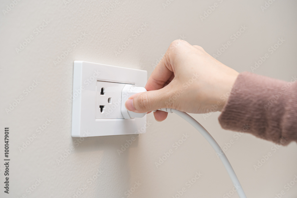 Hand of woman plugged in, unplugged electricity cord cable at home, put on or remove electric plug cable in socket on wall outlet for saving, control power electrical energy, eco environment concept. Hand of woman plugged in, unplugged electricity cord cable at home, put on or remove electric plug cable in socket on wall outlet for saving, control power electrical energy, eco environment concept.