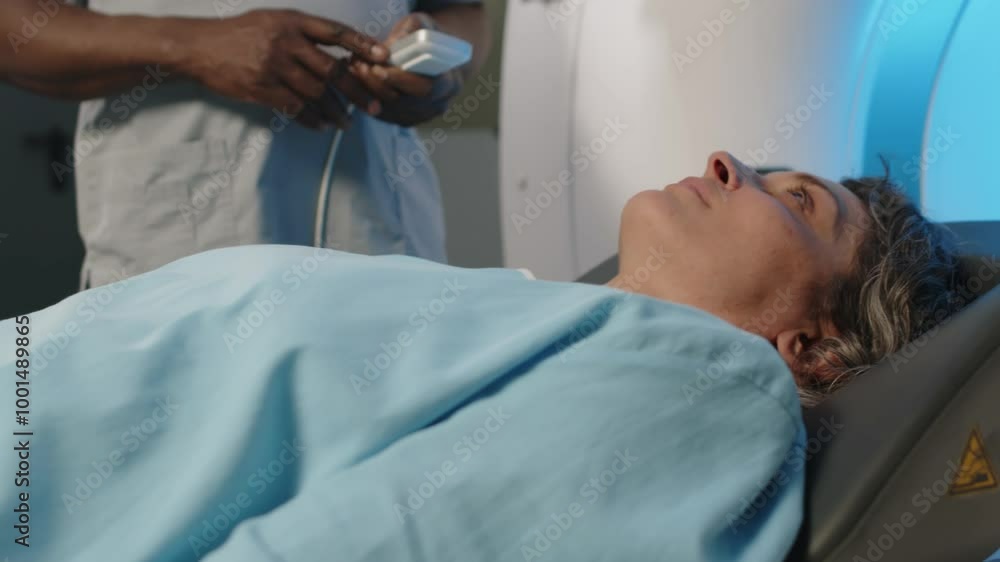 Mature Caucasian woman lying on CT scanner bed moving in opposite direction from gantry after finishing procedure Mature Caucasian woman lying on CT scanner bed moving in opposite direction from gantry after finishing procedure