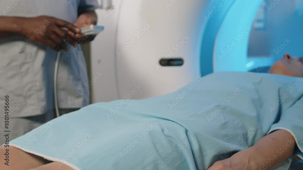 Mature Caucasian woman lying on CT scanner bed moving towards gantry, unrecognizable doctor controlling machine Mature Caucasian woman lying on CT scanner bed moving towards gantry, unrecognizable doctor controlling machine