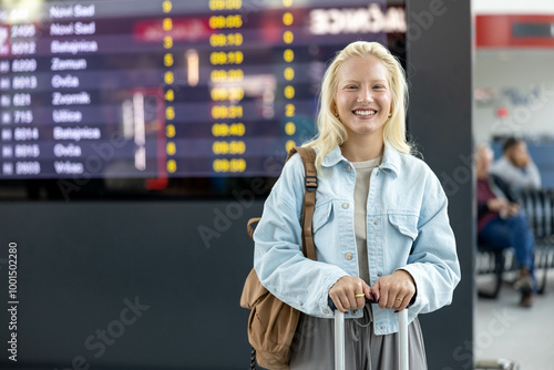 Konstfotografi A young woman stands confidently at the railway station terminal, suitcase handle in hand, preparing for her travel while showcasing a bright and reassuring smile