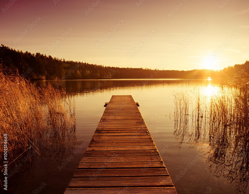 Obraz premium A serene wooden jetty stretches over a tranquil lake at sunsetin in a warm golden glow