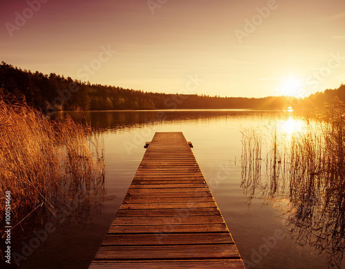 A serene wooden jetty stretches over a tranquil lake at sunsetin in a warm golden glow