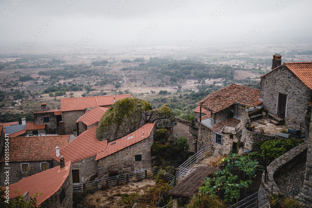 Obraz premium Portuguese houses in the village of Monsanto, Portugal, slowly disappearing into the fog as it descends into the valley, creating a peaceful and mystical scene.