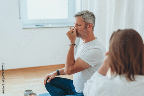 A man sitting in lotus position and a woman practicing alternate nostril breathing exercises during a meditation session photo