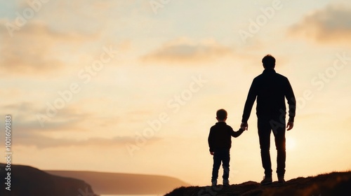 Father and son enjoy a sunset walk together on a grassy hill in early evening