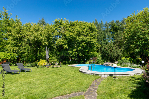 Swimming pool with sun beds on a closed private territory on a clear sunny day. Dense .greenery surrounds the territory.