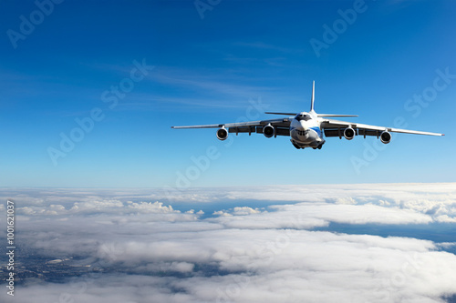 A cargo plane flying above the clouds in the blue and clear sky.