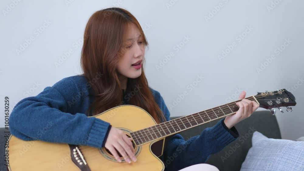 Young musician plays an acoustic guitar while sitting on a sofa, creating a relaxed and enjoyable atmosphere at home Young musician plays an acoustic guitar while sitting on a sofa, creating a relaxed and enjoyable atmosphere at home