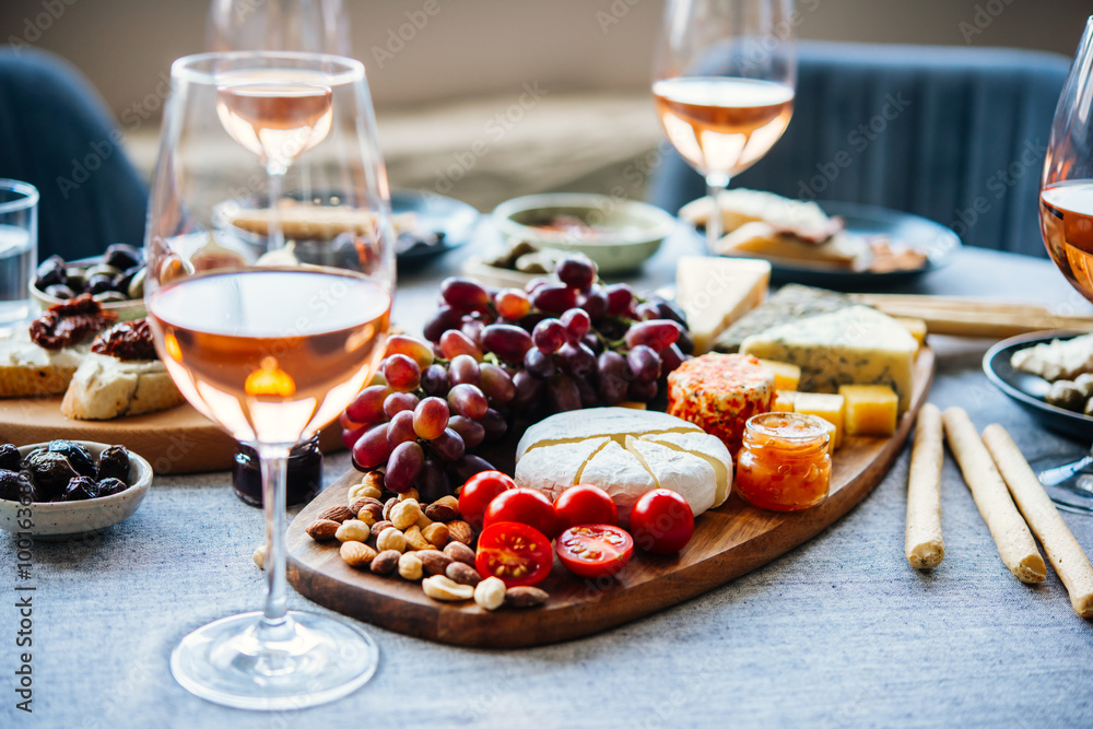 Wooden board with different kinds of cheese and glass of rose wine. Dinner or aperitivo party concept.