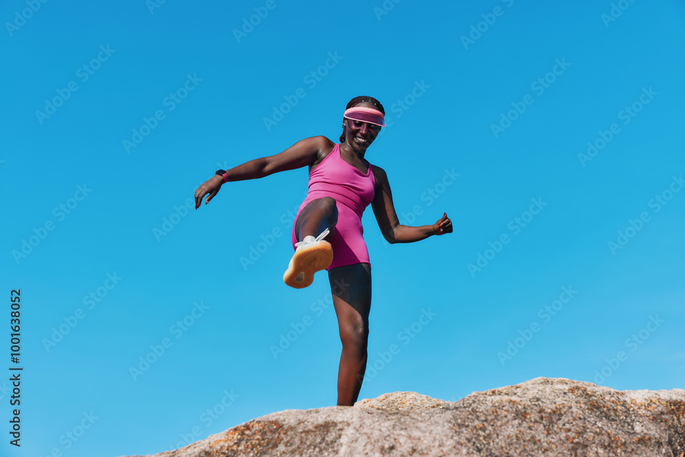 Young woman in pink athletic wear jumping on a rock against a bright blue sky Young woman in pink athletic wear jumping on a rock against a bright blue sky