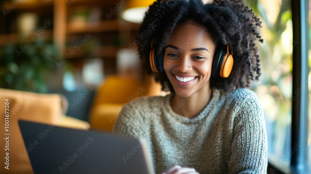 Smiling woman with curly hair working on a laptop while wearing headphones at a cozy café Smiling woman with curly hair working on a laptop while wearing headphones at a cozy café