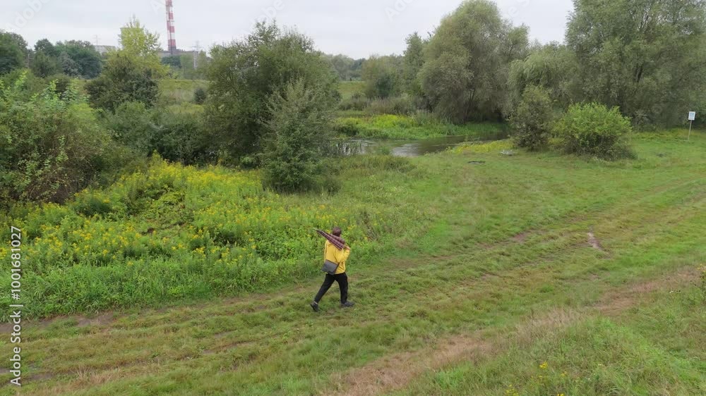 Dressed in a yellow raincoat, a man with an umbrella walks along a narrow path through nature during a rainy day. Relaxing outdoors, captured in slow motion. Dressed in a yellow raincoat, a man with an umbrella walks along a narrow path through nature during a rainy day. Relaxing outdoors, captured in slow motion.