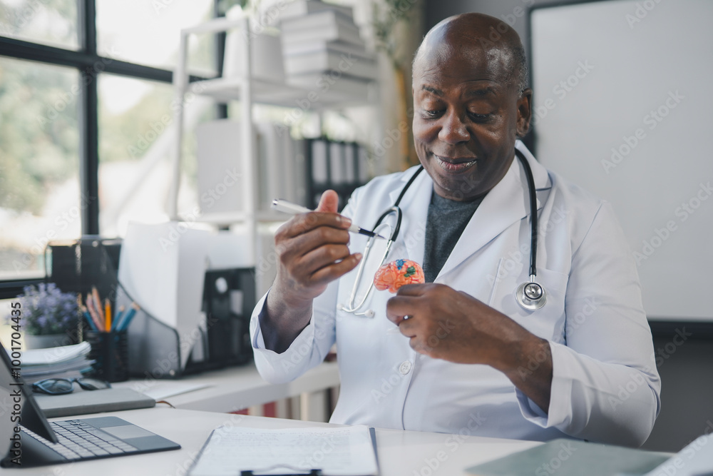 Smiling mature doctor explaining something using anatomical model of human brain in his bright modern office Smiling mature doctor explaining something using anatomical model of human brain in his bright modern office
