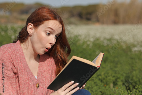 Photos Red-haired woman reads with great amazement an outdoor book