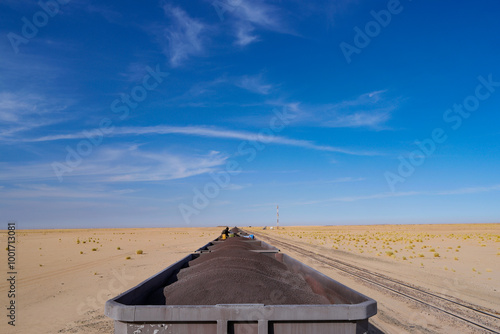 A freight train transporting iron ore across the vast desert landscape of Mauritania under a clear blue sky