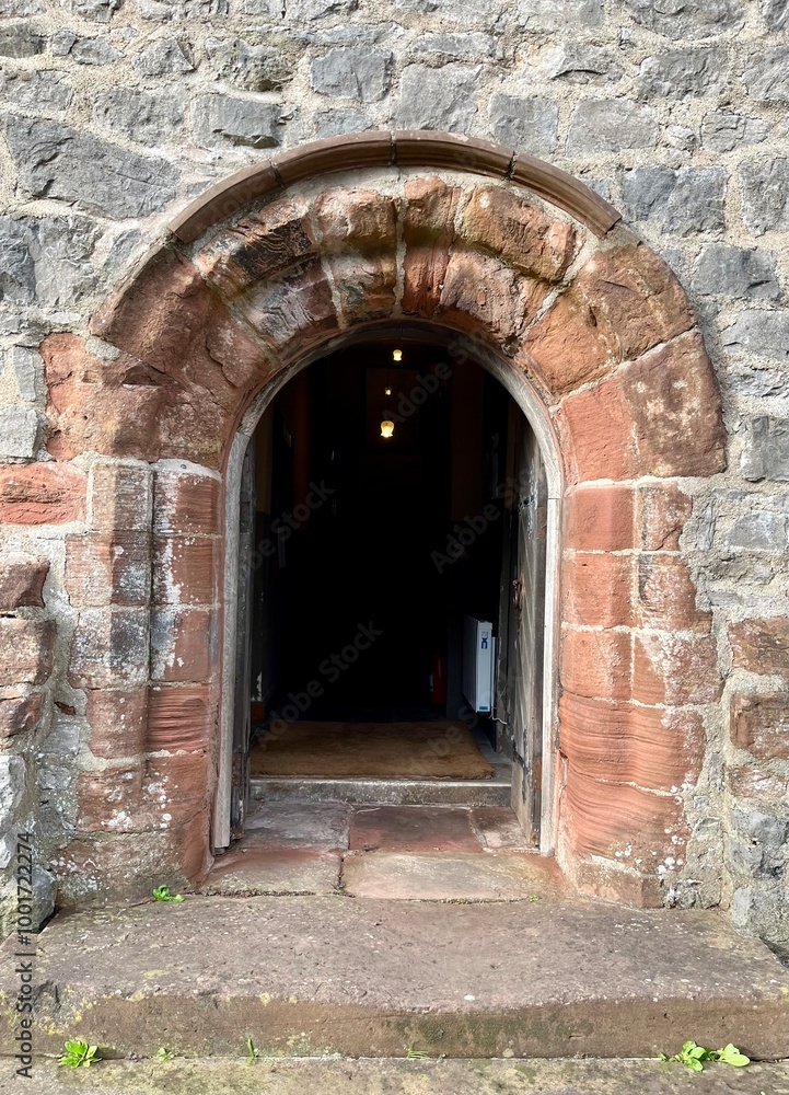 Fototapeta premium Dalton Castle, England. A weathered stone archway leading into a darkened interior, framed by ancient masonry. The worn steps add a historical charm, evoking a sense of mystery and the past.