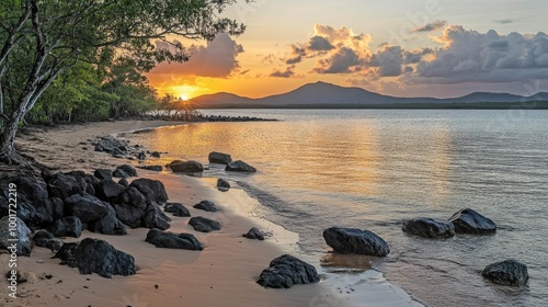A scenic sunset over a calm bay with a sandy beach, rocks, and lush green trees in the foreground.