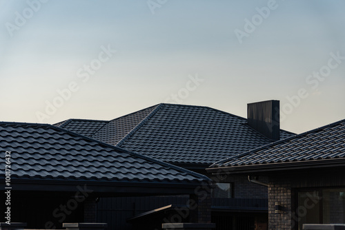 The rooftops of contemporary houses are silhouetted against a serene evening sky, highlighting their sleek design and tiles as the day transitions to night