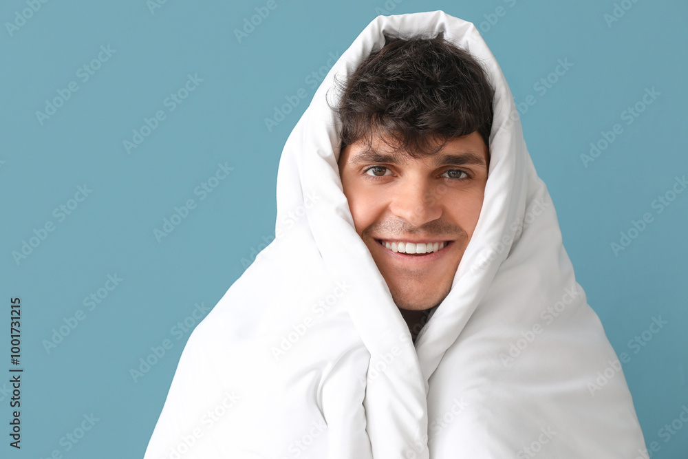 Handsome happy young man wrapped in soft blanket on blue background Handsome happy young man wrapped in soft blanket on blue background