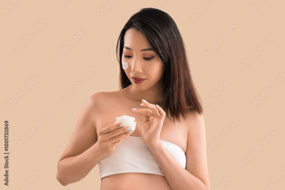 Beautiful Asian woman with facial cream on beige background Beautiful Asian woman with facial cream on beige background