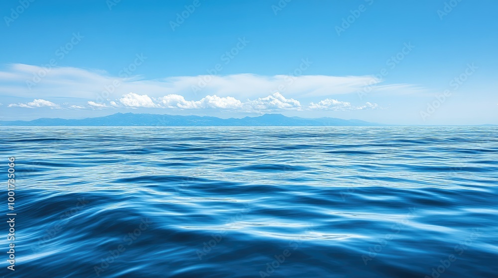 Fototapeta premium A tranquil blue ocean stretches out to the horizon, with a distant mountain range visible in the background under a clear sky.