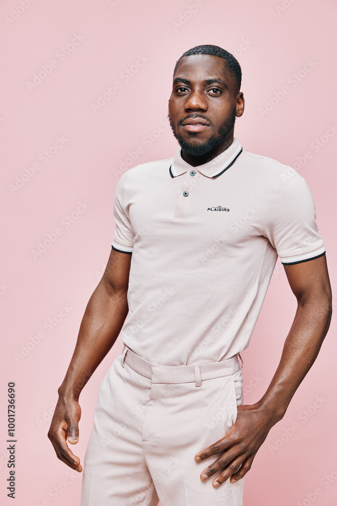 African male model in stylish light colored polo shirt, posing confidently against a soft pink background, showcasing contemporary fashion and self assured emotions African male model in stylish light colored polo shirt, posing confidently against a soft pink background, showcasing contemporary fashion and self assured emotions