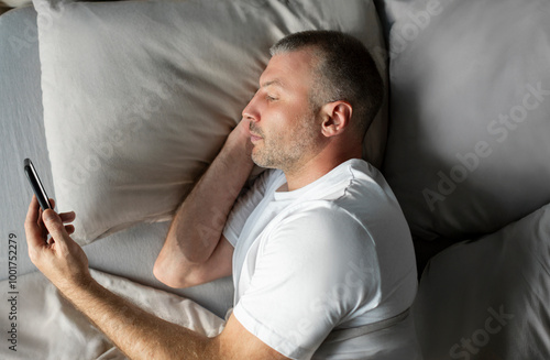 Man lying in bed and reading message on cellphone, texting or scrolling social media feed, above top view shot photo