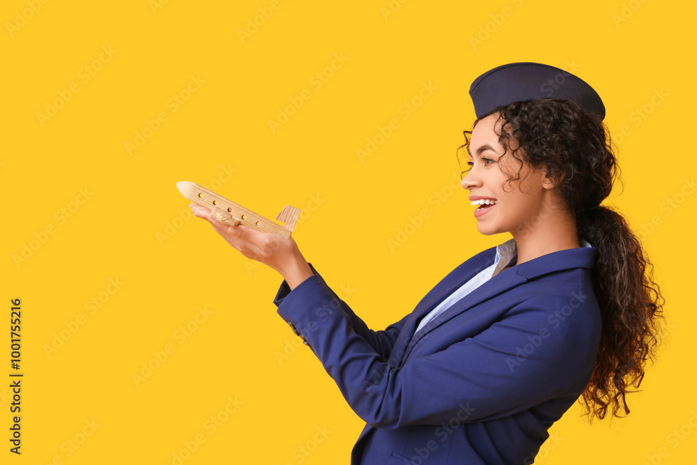 Beautiful African-American stewardess with toy plane on yellow background Beautiful African-American stewardess with toy plane on yellow background