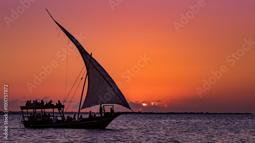 Voilier touristique naviguant devant le coucher de soleil avec le soleil se cachant derrière les nuages, Zanzibar, Tanzanie photo