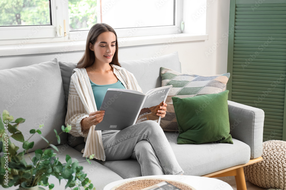 Young woman reading magazine on grey sofa in living room Young woman reading magazine on grey sofa in living room